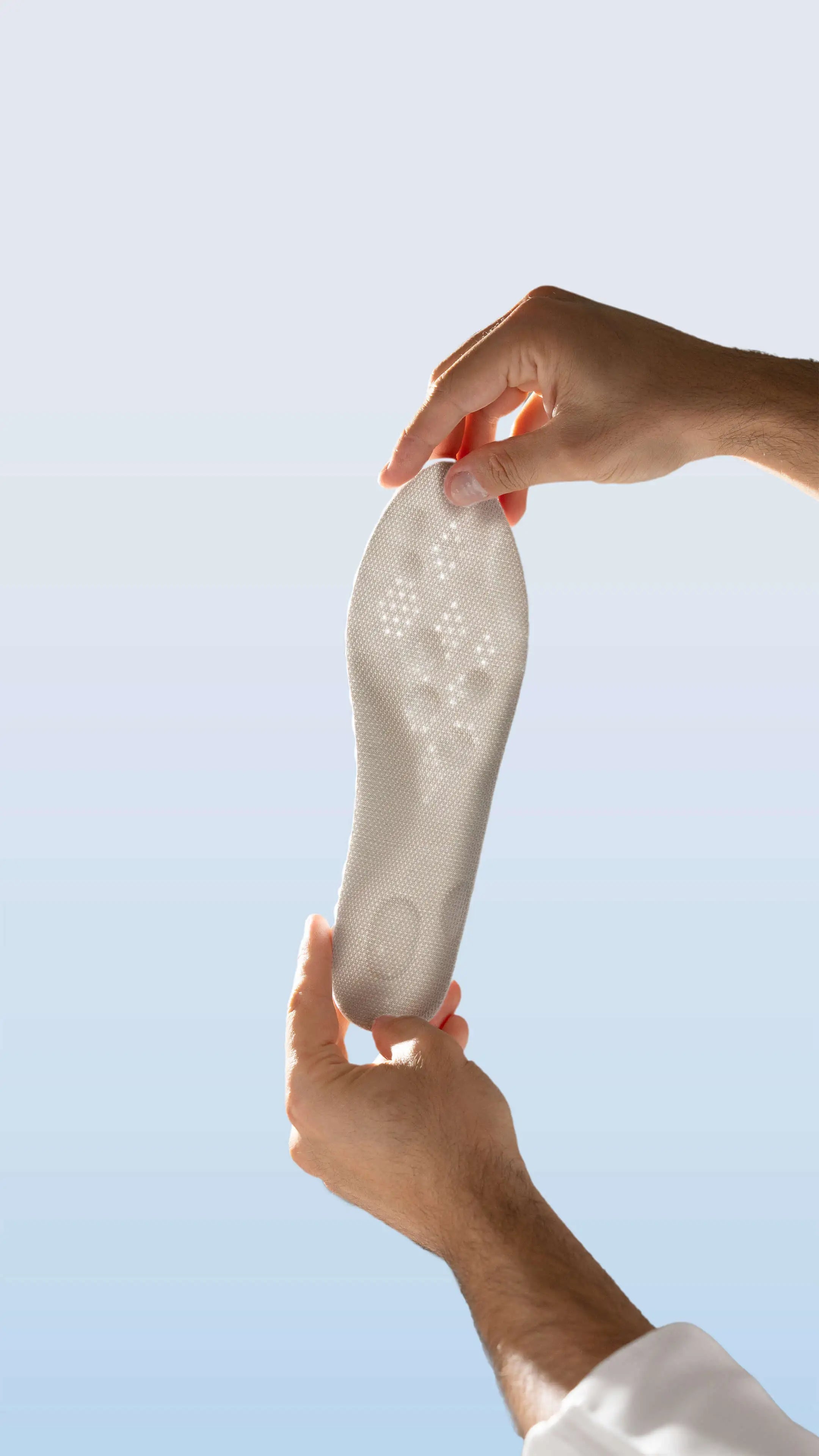 Person holding a white shoe insole against a clear blue sky